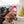 Load image into Gallery viewer, P.L.A.Y. Home for the Holidays Fur-Ever Naughty Toy - in mouth of big black dog looking to the side in front of a white bench with a gift bag and Christmas Tree pillows
