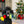 Load image into Gallery viewer, P.L.A.Y. Home for the Holidays Twinkly Tugger Toy - in the mouth of a smiling Black Poodle with a fireplace and a Christmas Tree in background
